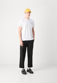 Camiseta blanca de algodón con mangas cortas, pantalones negros cortos, gorra amarilla y zapatos negros con un acento de correa. Conjunto simple y casual.