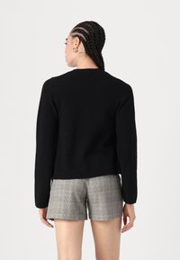 Μαύρος πλεκτός πουλόβερ με στρογγυλή λαιμόκοψη και μακριά μανίκια, συνδυασμένος με γκρι καρό σορτς. Η πίσω όψη δείχνει μήκος καλλιεργητή και απλή υφή.