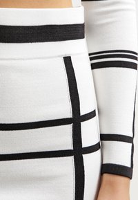 Tissu à rayures noir et blanc présentant un tricot texturé, avec des lignes horizontales et verticales distinctes formant un motif en grille.