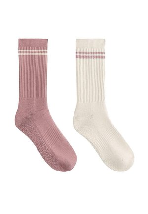 Une chaussette rose et une chaussette blanche à texture côtelée, chacune avec deux rayures horizontales près du bord supérieur et des grips en silicone sous la semelle.