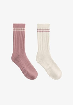 Jedna różowa skarpetka i jedna biała skarpetka o żebrowanej fakturze, każda z dwoma poziomymi paskami w pobliżu górnej mankiety oraz silikonowymi uchwytami na podeszwie.
