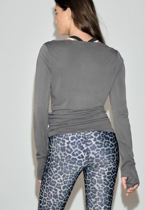 Woman wearing gray long-sleeve top and blue-gray leopard print leggings, shown from behind against a plain light background.