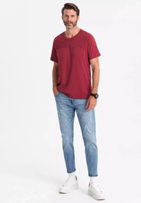 Bordová tričko s kapsou na hrudi, kombinované se světle modrými roztrhanými džínami a bílými teniskami. Casual design vhodný pro každodenní nošení.