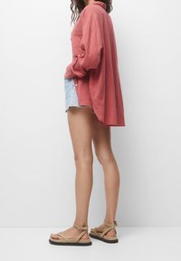 Lichte koraalkleurige blouse met lange mouwen en knoopdetails, gecombineerd met versleten denim shorts en tan gespen sandaaltjes met een platte zool.