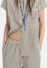 Camicetta a righe beige e blu con maniche corte e taschino frontale, abbinata a pantaloni larghi coordinati. Tessuto morbido con un design casual.