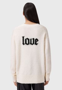 Kremowy, puszysty sweter z czarnym wzorem "love" z tyłu. Posiada długie rękawy i prążkowany dół. Miękka faktura.