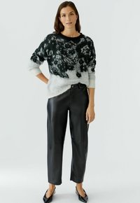 Schwarze Lederhosen mit entspannter Passform, kombiniert mit einem schwarz-weißen, abstrakt gemusterten Strickpullover mit rundem Halsausschnitt und gerippten Bündchen.