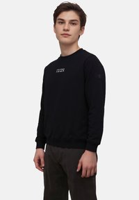 Zwarte sweatshirt van zacht materiaal, met een ronde hals en geribde manchetten. "JACK & JONES" logo gedrukt op de voorkant. Casual ontwerp.