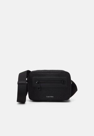 Sac bandoulière rectangulaire noir Calvin Klein avec bandoulière réglable, poche zippée à l'avant et motif de logo en relief discret.