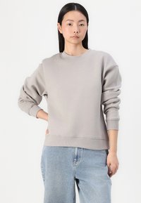Lysegrå sweatshirt med ribbestrikkede mansjetter og halslinning, løs passform og myk tekstur. Brukt sammen med lyseblå denimjeans.