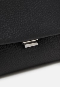 Detailní záběr černé texturované kožené peněženky se stříbrnou obdélníkovou sponou na bílém povrchu.