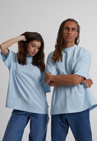 Camisetas de algodón azul claro con mangas cortas, corte relajado y cuello redondo. El diseño presenta un sutil logotipo en el pecho.