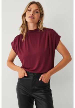 Bordeaux kortemou_sl_ev_t_op met hoge hals, zachte textuur en subtiele geplooide details op de schouders, gecombineerd met zwarte leren broek.