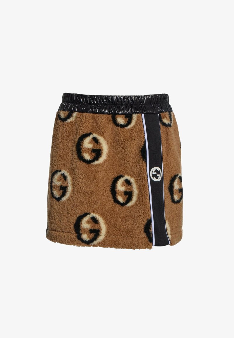 Mini-jupe marron duveteuse avec motifs circulaires noirs et beiges, taille élastique noire et bande noire verticale avec logo blanc sur le côté droit.