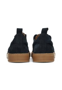 Zapatillas de ante azul marino con suelas de goma marrón, que presentan un diseño de corte bajo, tiradores en la parte trasera y detalles de costura minimalistas.