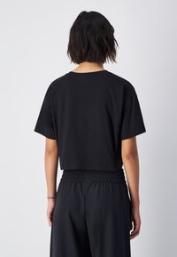 Camiseta negra corta con mangas cortas, cuello redondo y textura suave. Llevada con pantalones negros de cintura elástica a juego.