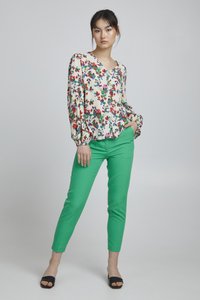 Bloemige blouse met lange, opgeblazen mouwen in roomwit, rood en groen. Groene slim-fit broek en zwarte open-toe schoenen maken de outfit compleet.