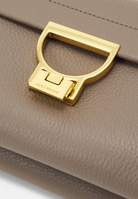 Leather handbag in taupe with a textured surface. Features a gold-tone metal clasp with a loop design and embossed branding.