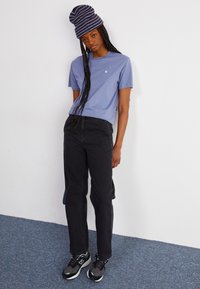 Korte mouw lichtblauw T-shirt, zwarte hoge taille jeans, gestreepte beanie en zwarte sneakers met grijze en witte details, staand tegen een effen achtergrond.
