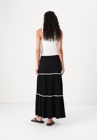 Jupe maxi noire avec un design à volants et des bordures blanches. Comprend une taille élastique et un tissu léger. Portée avec un débardeur blanc à côtes.