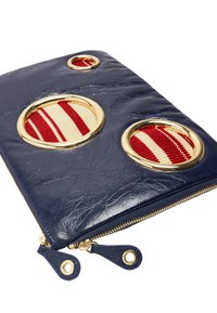 Granatowa torba z faux skóry z trzema okrągłymi wycięciami. Czerwono-biała materiałowa podszewka wewnątrz wycięć, złote akcenty i złote zamki błyskawiczne.