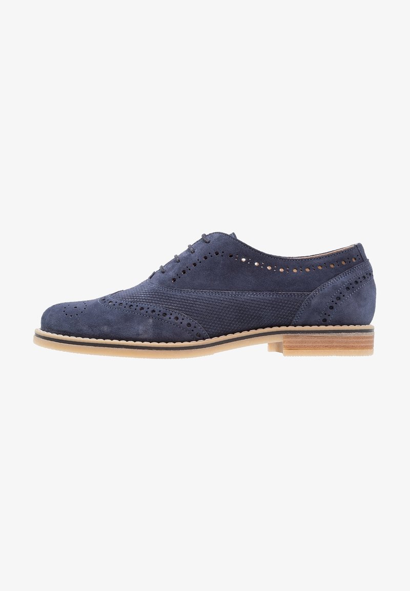 Chaussure brogue en daim bleu marine avec détails perforés, panneau latéral texturé, semelle beige, petit talon en bois empilé et fermeture à lacets.