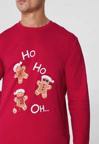 Rotes Langarm-T-Shirt mit drei Lebkuchenmännern, die Weihnachtsmützen tragen, einfachen Gesichtszügen und verspieltem weißen Text.