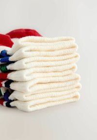 Sahnetonfarbige Socken, ordentlich gestapelt, mit einer weichen Textur und roten, blauen und grünen Akzenten an den oberen Kanten.