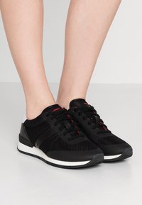 Baskets en mesh noires avec des accents rouges, bout rond, à lacets plats, semelle synthétique et talon rembourré.