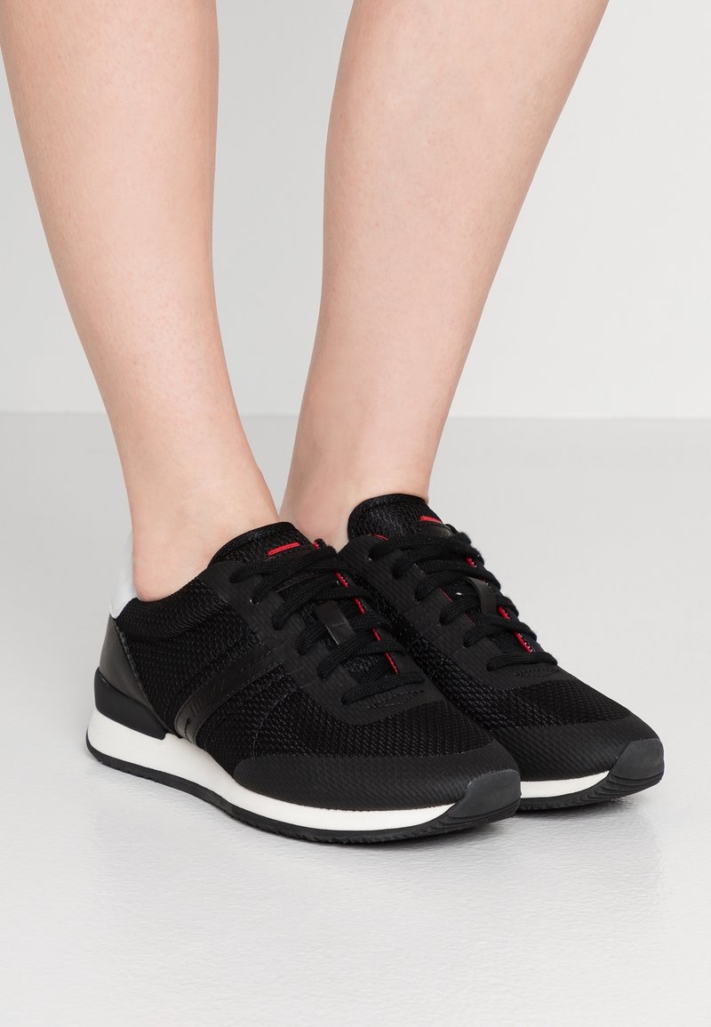 Baskets en mesh noires avec des accents rouges, bout rond, à lacets plats, semelle synthétique et talon rembourré.