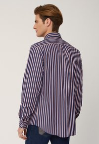 Camicia a maniche lunghe di colore blu navy con strisce verticali rosa, dotata di colletto standard e polsini abbottonati, realizzata in tessuto intrecciato.