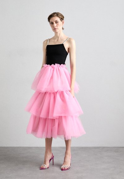 Zwart aansluitend topje met spaghettibandjes, gelaagde roze tule rok en roze hoge hakken met zilveren accenten, staande op een vlak oppervlak.