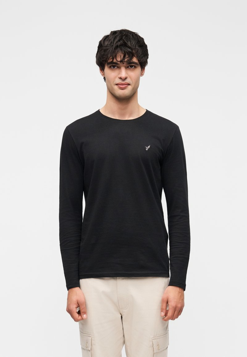 Μαύρο μακρυμάνικο μπλουζάκι με στρογγυλή λαιμόκοψη και μικρό λογότυπο στο στήθος, κατασκευασμένο από απαλό ύφασμα, συνδυασμένο με ανοιχτόχρωμο παντελόνι cargo.