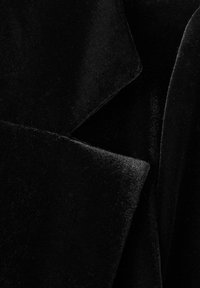 Tela de terciopelo negro con una textura suave. Presenta solapa y bordes doblados, creando una apariencia estructurada y en capas.
