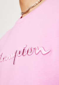 Růžové bavlněné tričko s vyšitým logem "Champion" v kontrastním odstínu růžové. Hladká struktura a kulatý výstřih.