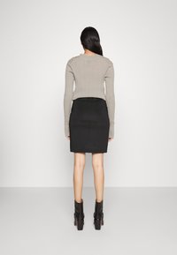 Grauer gerippter Langarmpullover mit Schulterdetails, kombiniert mit einem schwarzen Bleistiftrock. Das Model trägt schwarze High-Heel-Stiefel.