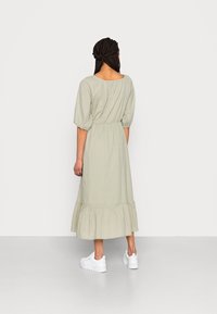 Světl zelené bavlněné šaty s krátkými nabíranými rukávy, elastickým pasem a vrstveným volánovým lemem. V kombinaci s bílými teniskami.