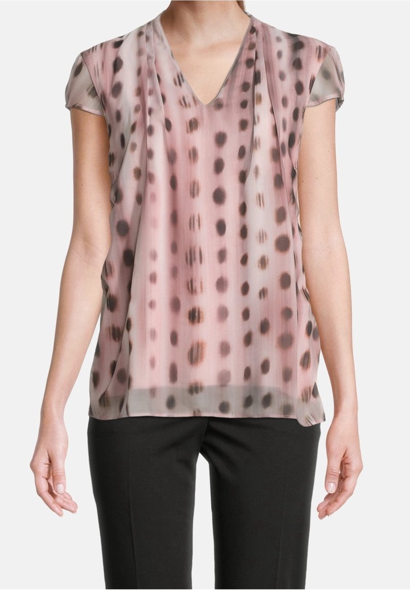 Blouse en voile rose avec un col en V et des manches courtes. Présente un motif à pois marron foncé. Coupe ample, tissu léger.