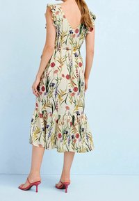 Bloemrijke midi-jurk met een V-rug, gerimpelde mouwen en een gelaagde zoom. Heeft een beige achtergrond met roze, paarse en groene patronen.