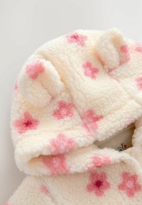 Une capuche en polaire douce avec de petites oreilles arrondies et des motifs floraux roses disséminés sur le tissu.