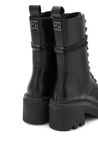 Melnas ādas potītes zābaki ar masīvu melnu zoli, aukliņu dizainu un dekoratīvu izšuvumu. Ietekmē logotipa akcentu uz papēža.