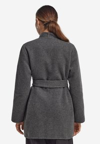 Grå ullrock med bälte i midjan och långa ärmar, med en enkel krage och slät textur. Sedd bakifrån.