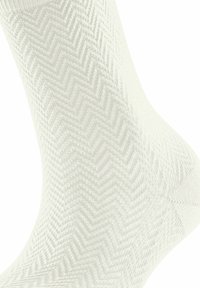 Chaussette blanche présentant une texture en chevrons, fabriquée en tissu tricoté avec un subtil éclat ; conçue pour un ajustement serré autour de la cheville.