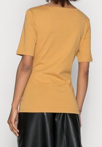 Musztardowa koszulka z krótkim rękawem i okrągłym dekoltem, wykonana z miękkiego materiału. Połączona z czarnymi spodniami o wysokim stanie przypominającymi skórę.