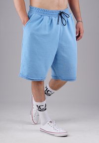 Light blue cotton shorts with an elastic waistband and drawstring. Features two side pockets and a relaxed fit. White sneakers and socks with black accents.