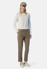 Maglietta a maniche lunghe crema con testo "NORTH SAILS", pantaloni verde oliva a gamba affusolata e sneaker beige-rossi con upper strutturato e dettagli in pizzo.
