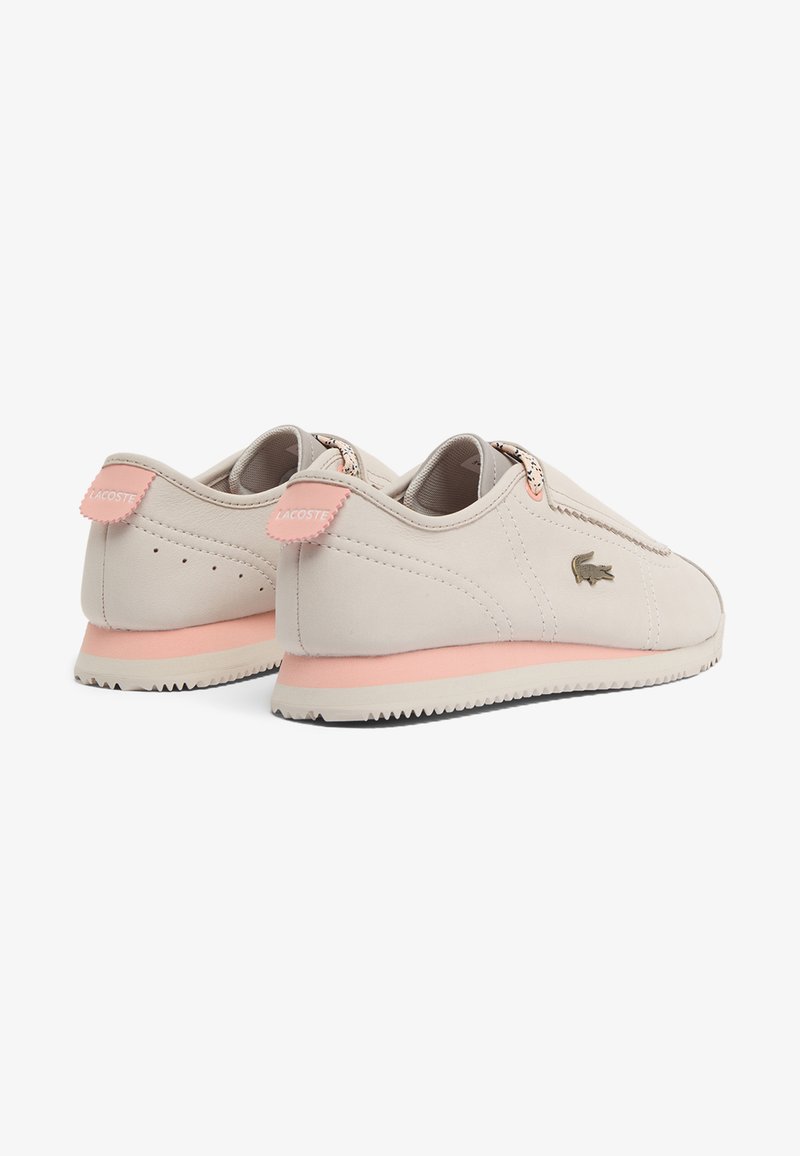 Paar beige flache Lacoste-Sneaker mit pinken Akzenten, Gummisohlen und Krokodillogo an der Seite, gezeigt aus Rücken- und Seitenansicht.