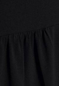 Zbliżenie na czarną tkaninę ze ściągniętym szwem tworzącym miękkie fałdy i teksturę.