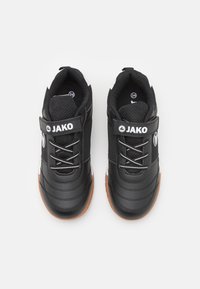 Baskets noires avec un dessus en synthétique texturé, des lacets élastiques et une bande Velcro. Semelle en caoutchouc avec des accents marron, présentant un logo sur le côté.