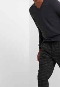 Maglione grigio scuro a V con maniche lunghe, abbinato a pantaloni da tuta a scacchi scuri con vita regolabile. Tessuto dalla superficie liscia.